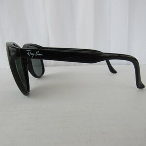 May include: Black Ray-Ban sunglasses with green lenses. The sunglasses have a classic aviator style with a thin metal frame and a curved lens.