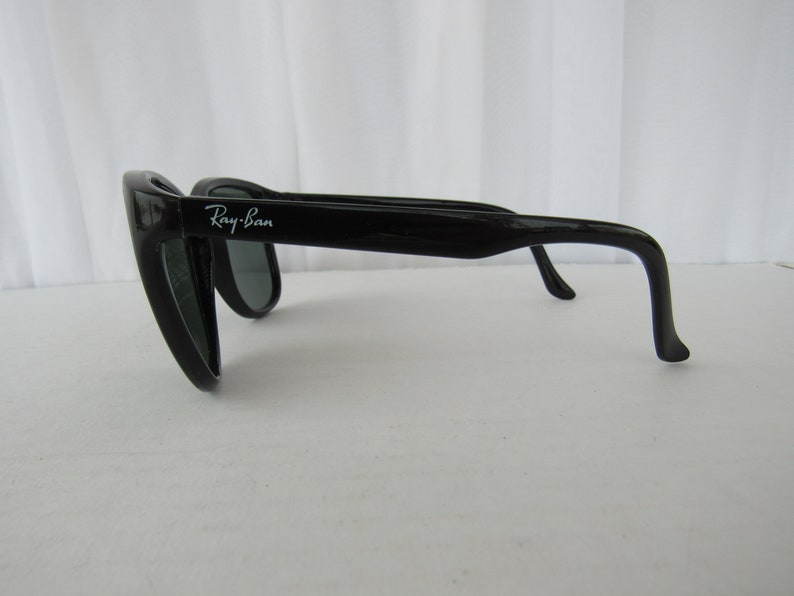 May include: Black Ray-Ban sunglasses with green lenses. The sunglasses have a classic aviator style with a thin metal frame and a curved lens.