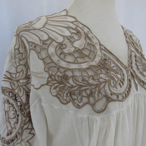 Puede incluir: Blusa color crema con intrincados bordados color canela alrededor del escote y los hombros. El bordado presenta un dise&ntilde;o floral y de encaje. La blusa tiene cuello en V y un ajuste holgado y fluido, lo que sugiere un estilo bohemio o vintage.