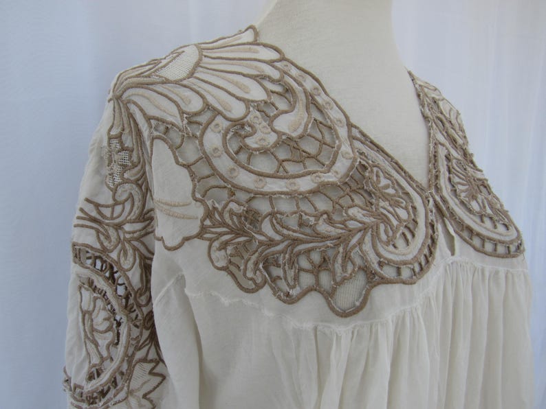 Puede incluir: Blusa color crema con intrincados bordados color canela alrededor del escote y los hombros. El bordado presenta un dise&ntilde;o floral y de encaje. La blusa tiene cuello en V y un ajuste holgado y fluido, lo que sugiere un estilo bohemio o vintage.