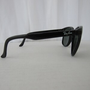 May include: Black Ray-Ban sunglasses with a curved frame and dark lenses.