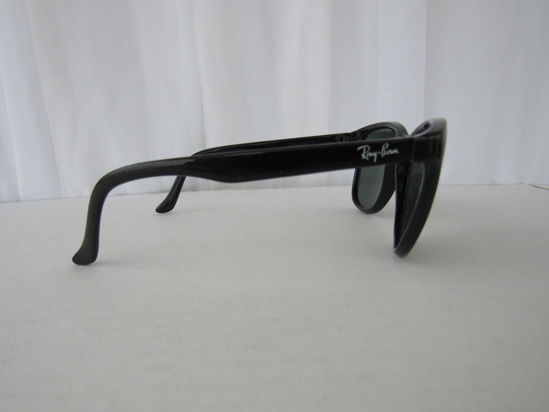 May include: Black Ray-Ban sunglasses with a curved frame and dark lenses.
