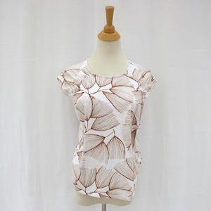 May include: A white top with a brown leaf pattern. The short-sleeved shirt has a scoop neck and is displayed on a mannequin. The leaf design is repeated across the entire shirt.
