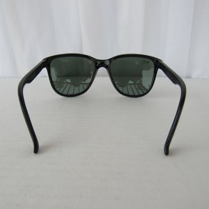 May include: Black sunglasses with dark green lenses. The sunglasses have a classic, retro style.
