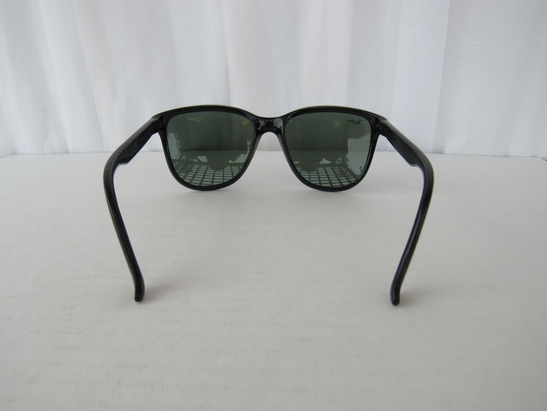May include: Black sunglasses with dark green lenses. The sunglasses have a classic, retro style.