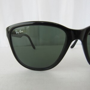 May include: Black Ray-Ban sunglasses with green lenses. The sunglasses have a sleek, modern design.
