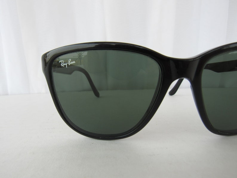 May include: Black Ray-Ban sunglasses with green lenses. The sunglasses have a sleek, modern design.