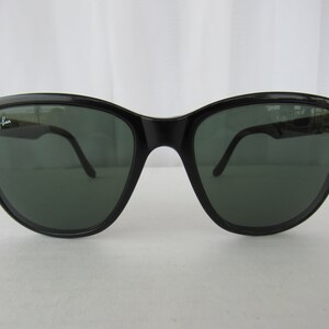 May include: Black Ray-Ban sunglasses with green lenses. The sunglasses have a cat-eye shape.