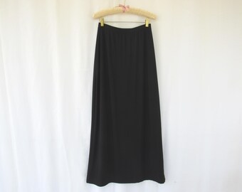 May include: A long, black skirt hangs from a wooden hanger with a pink ribbon. The skirt is made of a smooth, flowing fabric and has a simple, elegant design. The skirt is a solid black color.