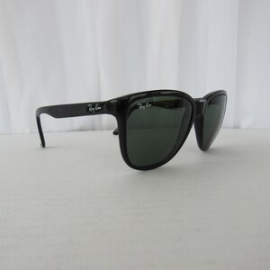 May include: Black Ray-Ban sunglasses with green lenses. The sunglasses have a classic, angular shape.