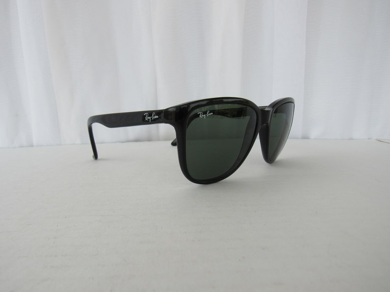 May include: Black Ray-Ban sunglasses with green lenses. The sunglasses have a classic, angular shape.