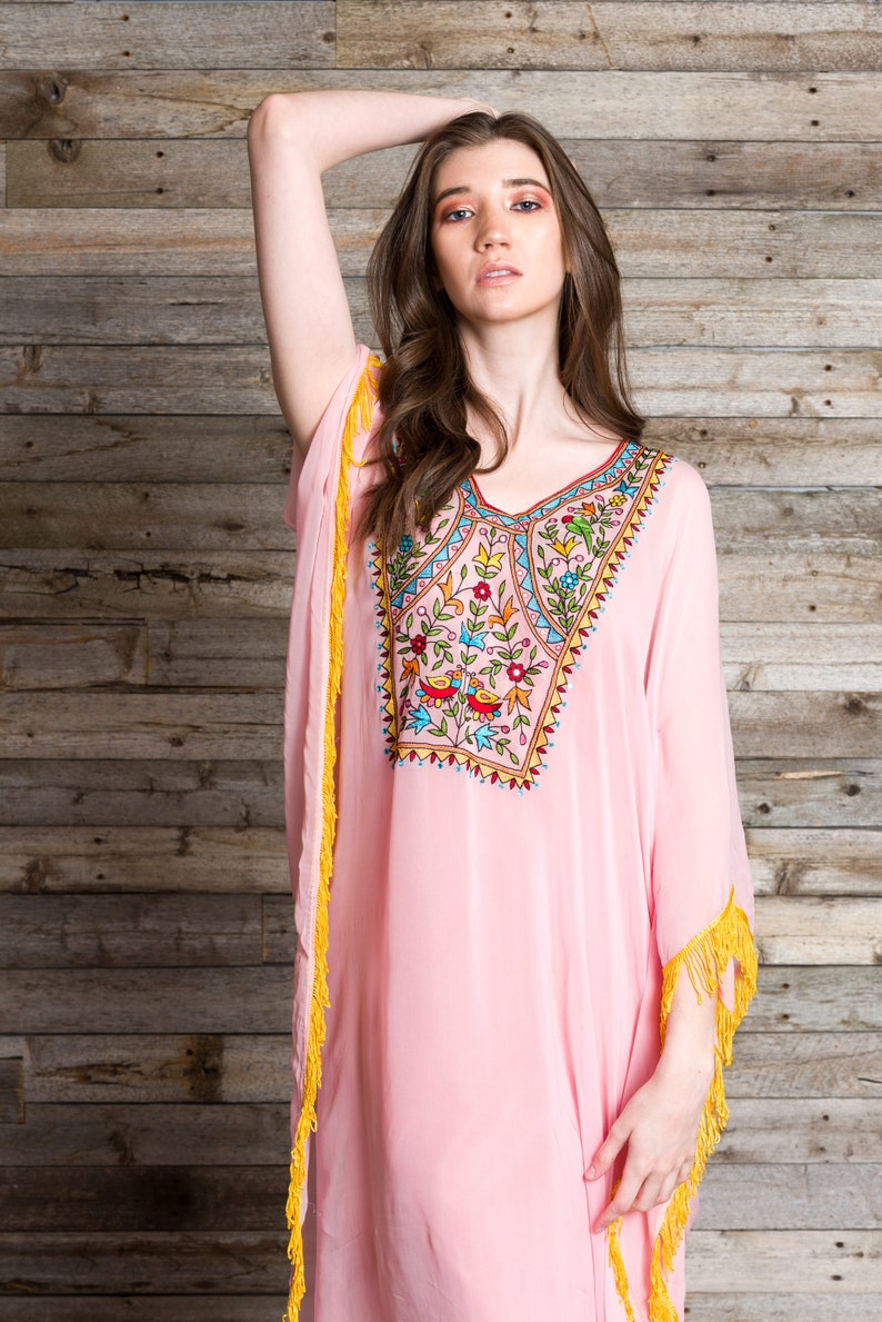 May include: A pink, long-sleeved kaftan with yellow fringe trim and colourful embroidery featuring flowers and birds.