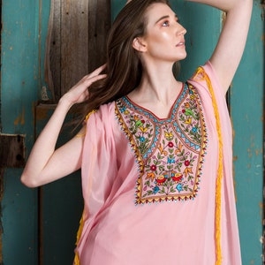 May include: A pink, sheer, long-sleeved dress with colourful embroidery featuring flowers and birds. The dress has yellow tassels on the sleeves and hem.