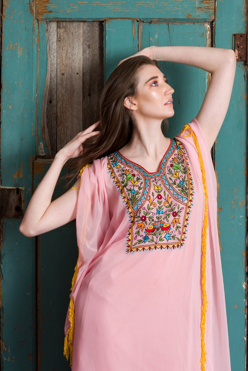 May include: A pink, sheer, long-sleeved dress with colourful embroidery featuring flowers and birds. The dress has yellow tassels on the sleeves and hem.