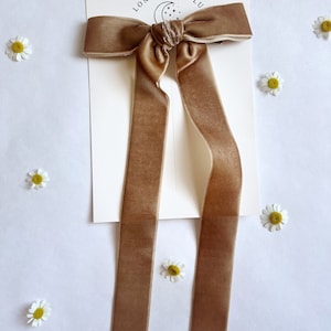 May include: A brown velvet hair bow with long tails. The bow is tied in a simple knot and the tails are straight. The bow is on a white background with a card that says "London & Lulu".