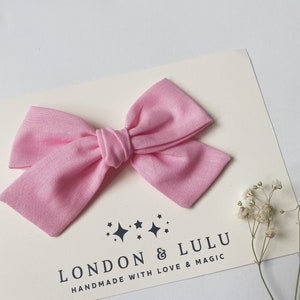 May include: A pink fabric bow with a white background featuring the text "LONDON & LULU HANDMADE WITH LOVE & MAGIC".