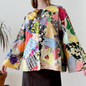 May include: A patchwork jacket with a vibrant mix of floral, striped, and solid fabric patches in various colors. The jacket has a round collar and button closure. The model is wearing a black skirt.