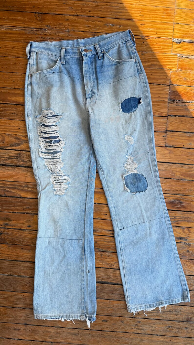 Op de afbeelding: Lichtblauwe spijkerbroek met distressed details. De jeans heeft gescheurde delen aan de voorkant van de benen en patches. De jeans heeft een klassiek ontwerp met vijf zakken en een uitlopende beenopening.