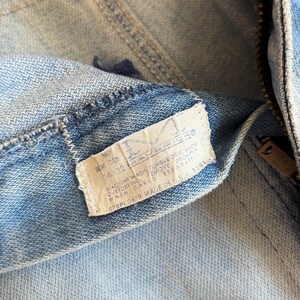 Op de afbeelding: Close-up van een lichtblauwe denim jeans met een zichtbaar label. Het label geeft de maat 36x32 aan en bevat wasinstructies. De jeans heeft een rits en een knoopsluiting.