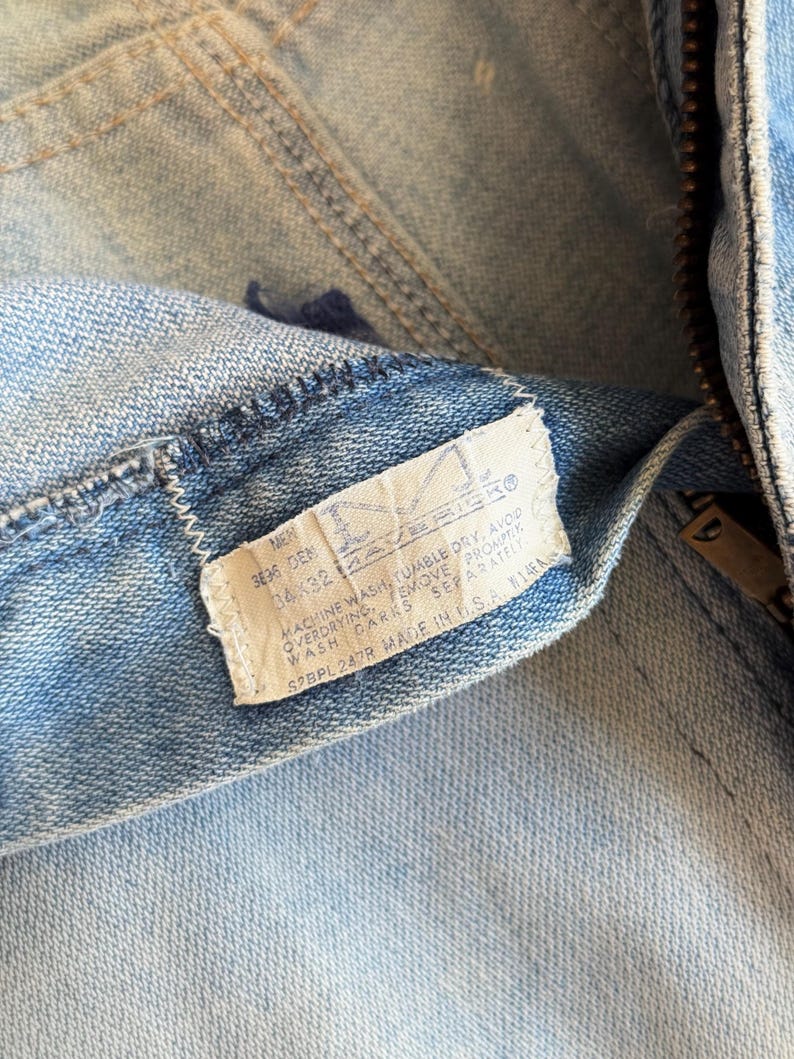 Op de afbeelding: Close-up van een lichtblauwe denim jeans met een zichtbaar label. Het label geeft de maat 36x32 aan en bevat wasinstructies. De jeans heeft een rits en een knoopsluiting.