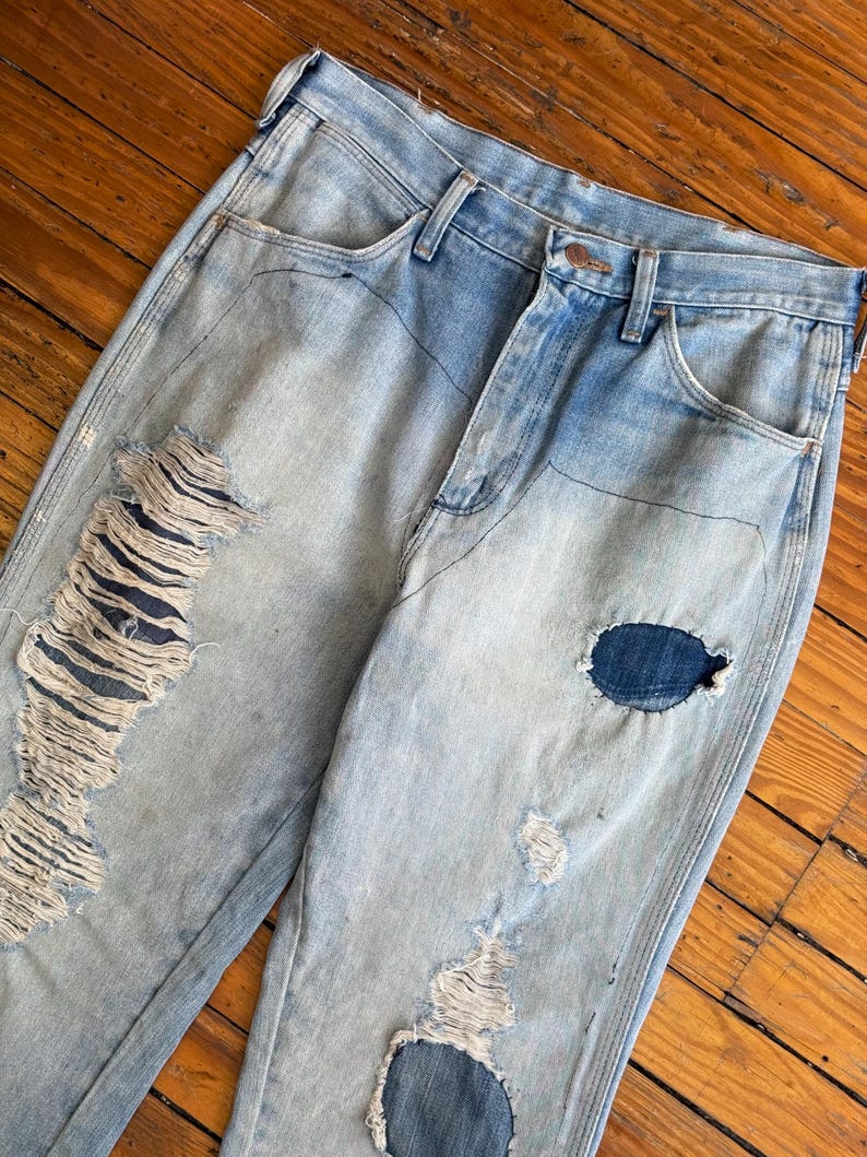 Op de afbeelding: Lichtblauwe denim jeans met distressed details, waaronder grote scheuren en patches. De jeans hebben een klassiek ontwerp met vijf zakken en een knoop- en ritssluiting. De denim heeft een vervaagde wassing.