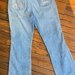 Op de afbeelding: Lichtblauwe jeans met een distressed design. De jeans hebben een klassiek ontwerp met vijf zakken, een hoge taille en een uitlopende pijp. De achterzakken hebben een uniek gestikt ontwerp. De jeans vertonen tekenen van slijtage, wat bijdraagt aan hun vintage uitstraling.