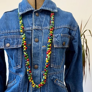 May include: A denim jacket with a colorful beaded necklace. The necklace features a variety of small, round beads in shades of red, yellow, green, and blue. The jacket has a classic design with pockets and button closures.