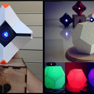 Könnte beinhalten: Eine weiße, geometrische Destiny Ghost-Hülle mit zentralem blauen Licht, präsentiert neben einer Holzbox. Weitere Bilder zeigen eine weiße Dodekaeder-Lampe mit komplexen Mustern, die in Grün, Rot, Lila und Blau mit einer Fernbedienung leuchtet.