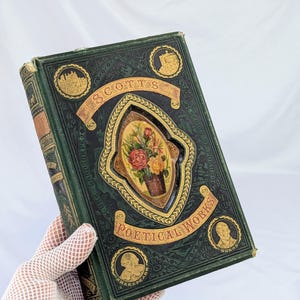 May include: A dark green hardcover book titled Scott's Poetical Works with gold embossed lettering and decorative borders. The cover features a central oval inlay depicting a colorful floral bouquet and four circular portraits of historical figures.