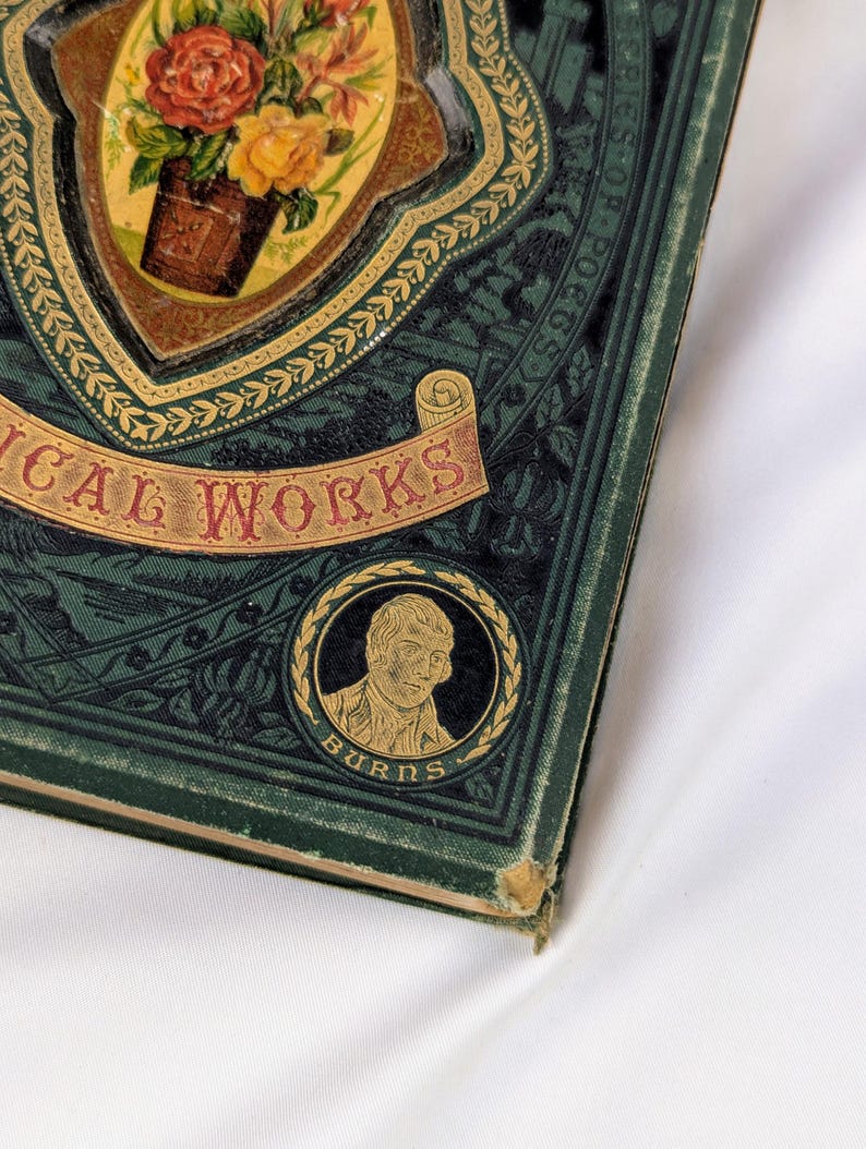 May include: A dark green hardcover book titled POETICAL WORKS with gold embossed lettering and decorative borders. The cover features a central oval illustration of a flower bouquet and a circular portrait of a man labeled BURNS at the bottom.