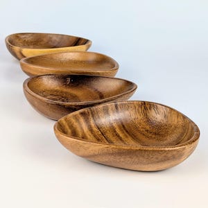 Könnte beinhalten: Ein Set aus vier tropfenförmigen Holzschalen, die in einer diagonalen Linie angeordnet sind. Jede Schale hat eine glatte, polierte Oberfläche mit einer ausgeprägten braunen Holzmaserung und natürlichen Farbvariationen in Brauntönen.