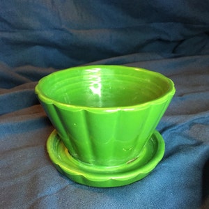May include: A green ceramic planter with a fluted design and a matching saucer. The planter is empty and ready for a plant.