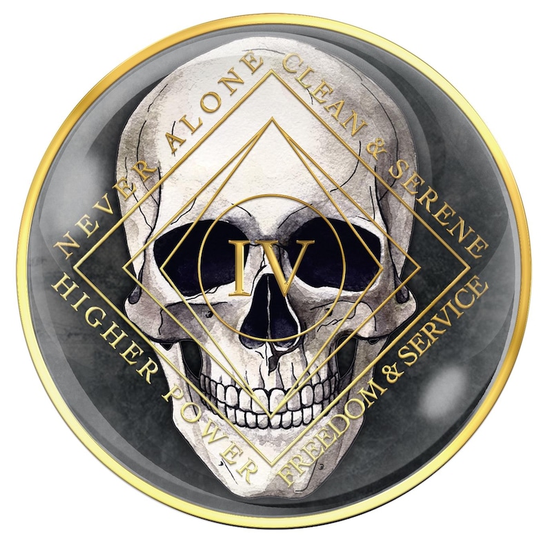 May include: A round, dark gray and gold-toned emblem featuring a detailed skull illustration. The skull is centered within a gold geometric design, with the Roman numeral IV. The words "NEVER ALONE", "CLEAN & SERENE", "HIGHER POWER", and "FREEDOM & SERVICE" are inscribed.