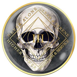 May include: A round, gold-rimmed emblem featuring a detailed skull illustration. The skull is centered within a gold geometric design, with the Roman numeral "III" in gold. The outer ring includes the words "NEVER ALONE", "CLEAN & SERENE", "FREEDOM & SERVICE", and "HIGHER POWER".