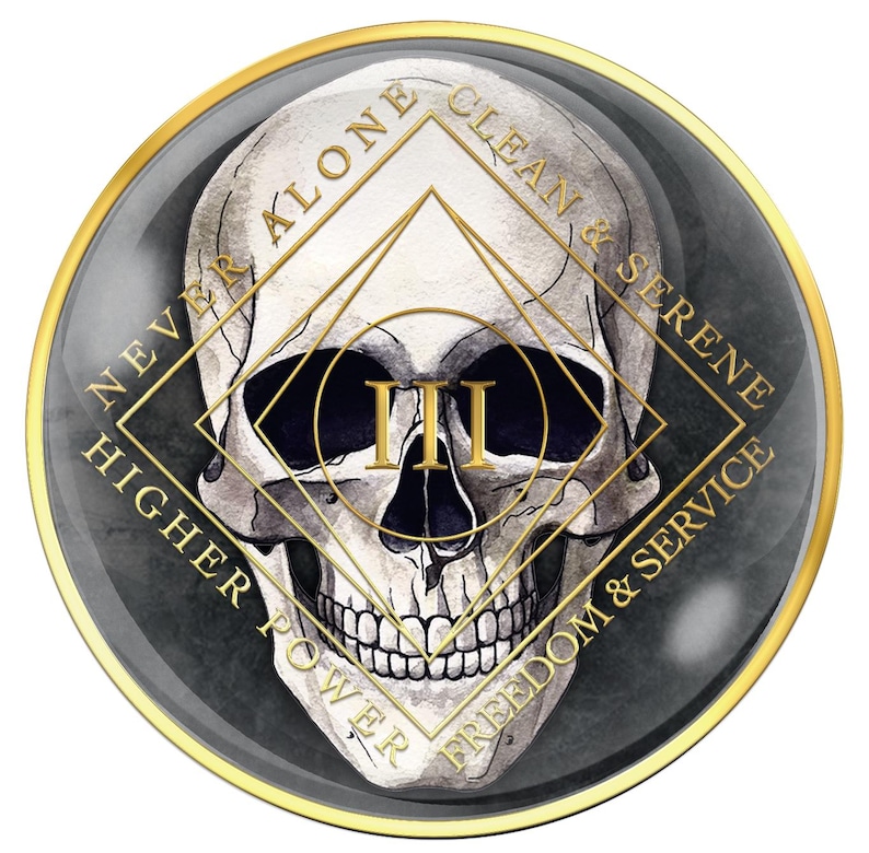 May include: A round, gold-rimmed emblem featuring a detailed skull illustration. The skull is centered within a gold geometric design, with the Roman numeral "III" in gold. The outer ring includes the words "NEVER ALONE", "CLEAN & SERENE", "FREEDOM & SERVICE", and "HIGHER POWER".