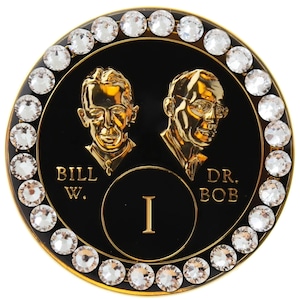 May include: A round black and gold coin with a white rhinestone border. The coin features two portraits of men with the text "BILL W." and "DR. BOB" and the Roman numeral "I" in the centre.