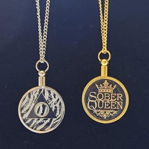Puede incluir: Dos collares con colgantes redondos. Uno tiene un triángulo negro con las palabras "Recovery" y "Unity" y un fondo de estampado de cebra. El otro tiene las palabras "Sober Queen" con un diseño de corona.