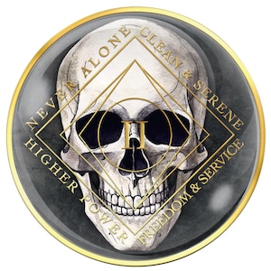 May include: A round, dark gray and gold-rimmed emblem featuring a detailed skull illustration. Gold text encircles the skull, reading "NEVER ALONE, CLEAN & SERENE, FREEDOM & SERVICE, HIGHER POWER." A gold diamond shape is centered on the skull.
