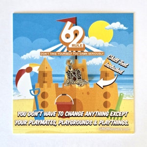 Op de afbeelding: Een kleurrijke kaart met een strandscene en de tekst "62 Rule Don't take yourself too damn seriously." De kaart toont een zandkasteel met een bedel eraan bevestigd. De bedel is een klein zilveren kasteel met een rood dak. De tekst "Chill Tool Included" staat op de kaart.