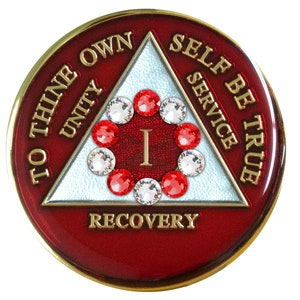 May include: Red and gold sobriety coin with a white triangle in the center. The triangle has the words "To Thine Own Self Be True" written around it. The words "Unity", "Service", and "Recovery" are written on the triangle. The coin has a circle of red and clear rhinestones in the center.