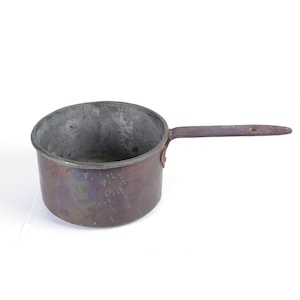 Puede incluir: Una cacerola de cobre vintage con un mango de madera. La cacerola tiene una pátina desgastada y envejecida y está ligeramente deslustrada.