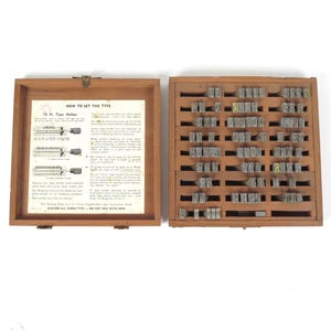 May include: A wooden storage box containing metal letterpress type pieces organized in rows. The lid interior features a printed instruction sheet titled HOW TO SET THE TYPE, detailing the use of an 18 Pt. Type Holder for stamping tasks.
