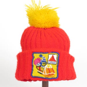 May include: Red knit beanie with a yellow pom pom and a blue and yellow embroidered patch featuring a cartoon bee riding a snowmobile with the text "CITGO" on it.