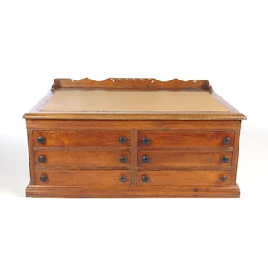 May include: A wooden drawer cabinet with a brown leather top and six drawers. Each drawer has black metal knobs.