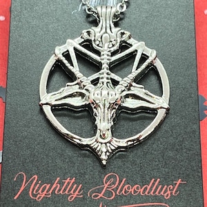 Peut inclure: Collier pendentif argent&eacute; avec un design de pentagramme d&eacute;taill&eacute; et une t&ecirc;te de ch&egrave;vre au centre. Le collier est suspendu &agrave; une cha&icirc;ne d&eacute;licate. Le texte "Nightly Bloodlust" est visible sur le fond noir.