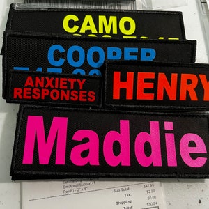May include: A stack of black fabric patches with various colored text. The patches read "Ask to Pet", "Camo", "Cooper", "Anxiety Responses", "Henry", and "Maddie".