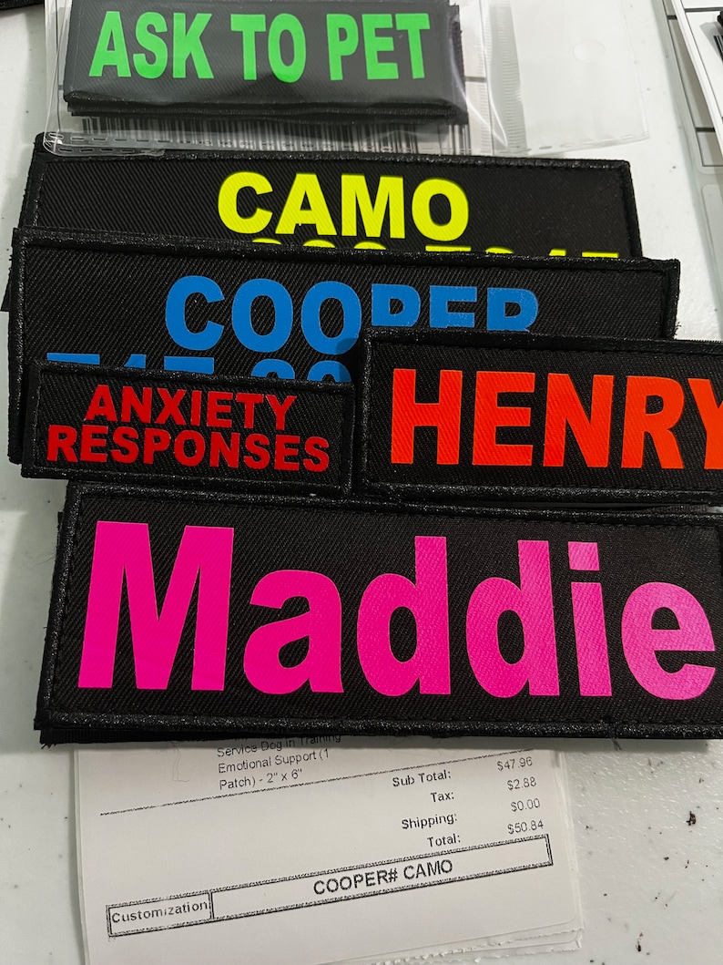 May include: A stack of black fabric patches with various colored text. The patches read "Ask to Pet", "Camo", "Cooper", "Anxiety Responses", "Henry", and "Maddie".