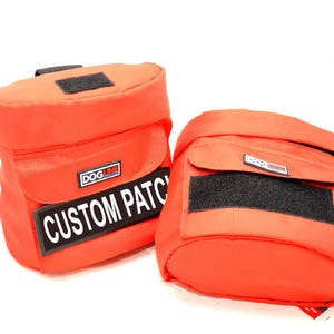May include: Two vibrant orange pouches with black velcro patches and a rectangular flap. One pouch features a label that reads "CUSTOM PATCH". These pouches are likely designed for carrying items.
