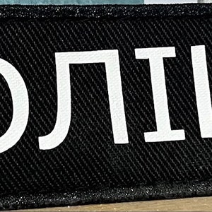 Może przedstawiać: Czarny naszywka z białym tekstem, kt&oacute;ry brzmi "ПОЛИЦИЯ", co jest rosyjskim słowem oznaczającym "Policja".