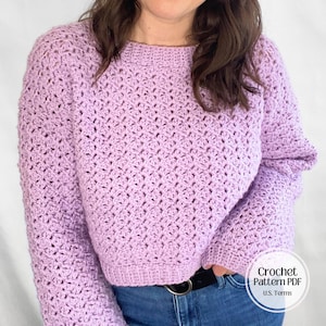 Könnte beinhalten: Ein helllila Häkelpullover mit langen Ärmeln. Der Pullover hat ein strukturiertes Stichmuster und gerippte Säume und Bündchen. Der Text "Crochet Pattern PDF U.S. Terms" befindet sich in der unteren rechten Ecke.